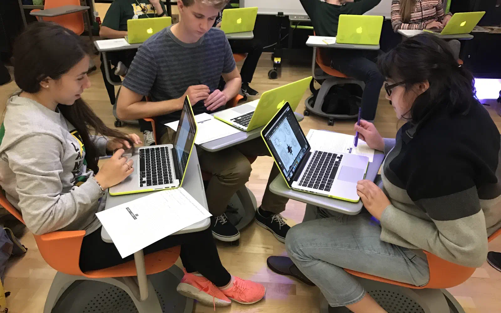 Four students around a table, each working on a laptop.
