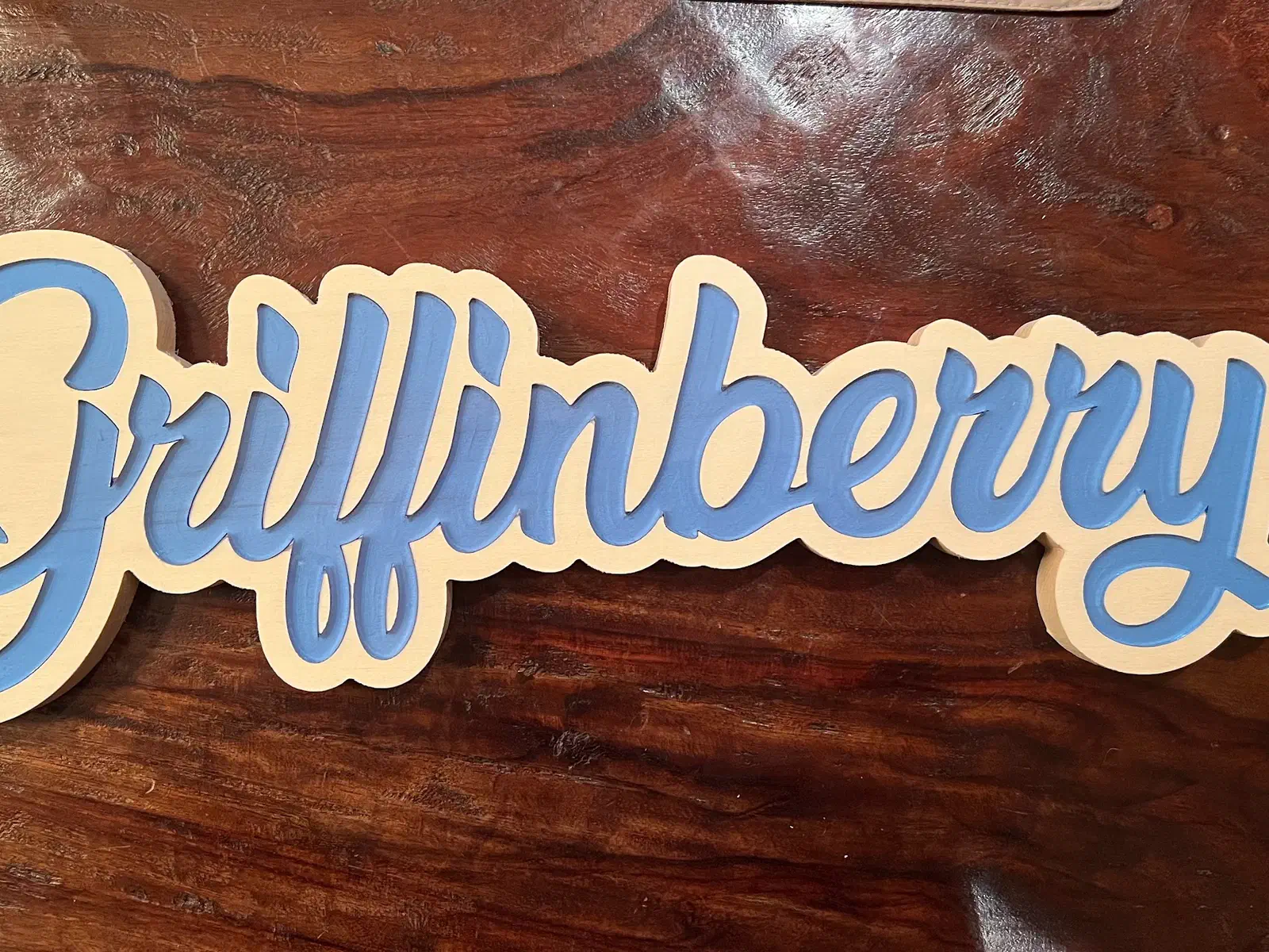 The word Griffinberry cut in a bold script from light wood, lying on a dark walnut board.
