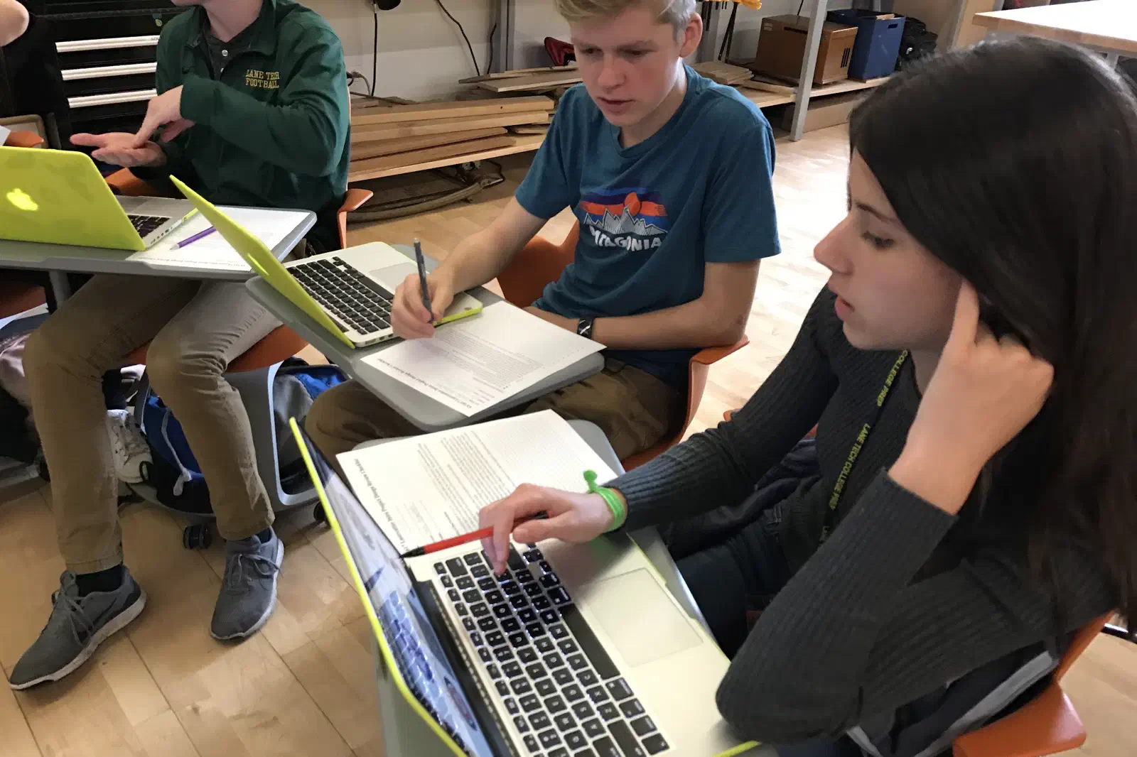 Two students designing on laptops at a desk in a classroom.