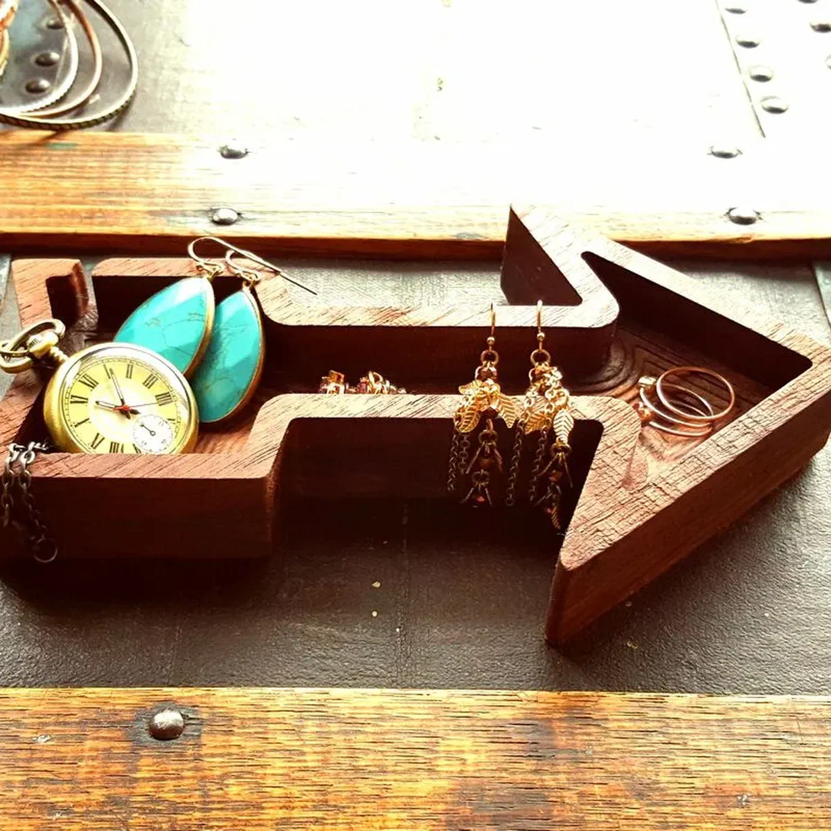 A walnut arrow-shaped dish holding jewelry and a pocket watch.