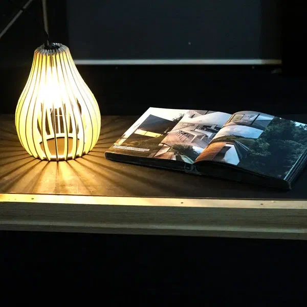 A slatted hanging lamp lighting a magazine on a table in a dark room.