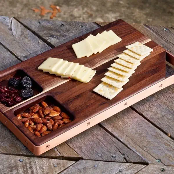 A walnut serving board with cheese, crackers, nuts and fruit arranged on it.
