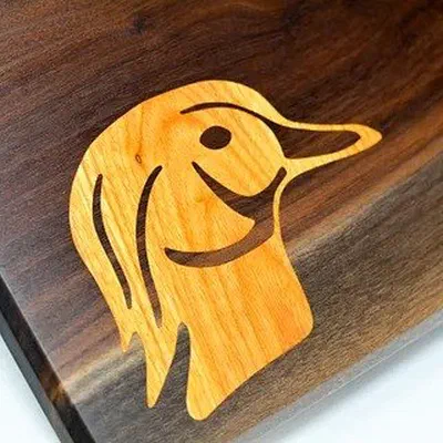 A duck head inlaid in pale wood into a dark live-edge board.