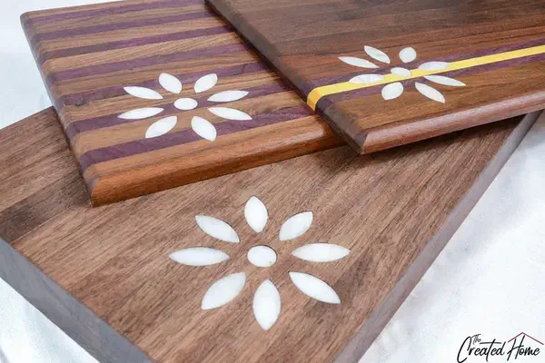A finished dark wooden cutting board with pale flower-shaped marble inlays