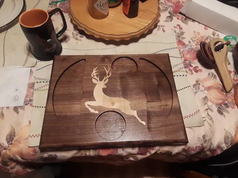 A finished dark wooden board with curved side pockets, two round recesses and a pale deer inlay