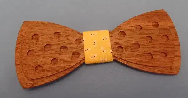 A complete walnut bow tie with recessed dots and a yellow fabric center on an uncluttered gray background.