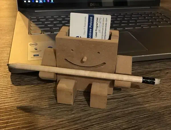 A smiling plywood figure holding business cards behind its face and a pencil across its arms