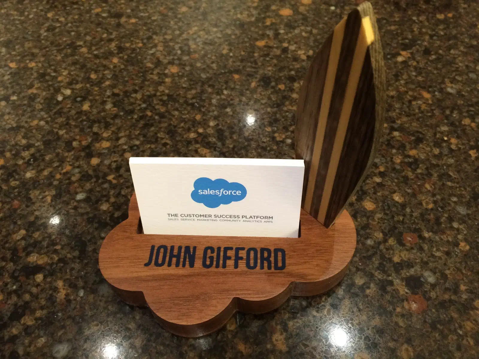 A wooden business card holder with a striped surfboard, a scalloped base and blue name lettering
