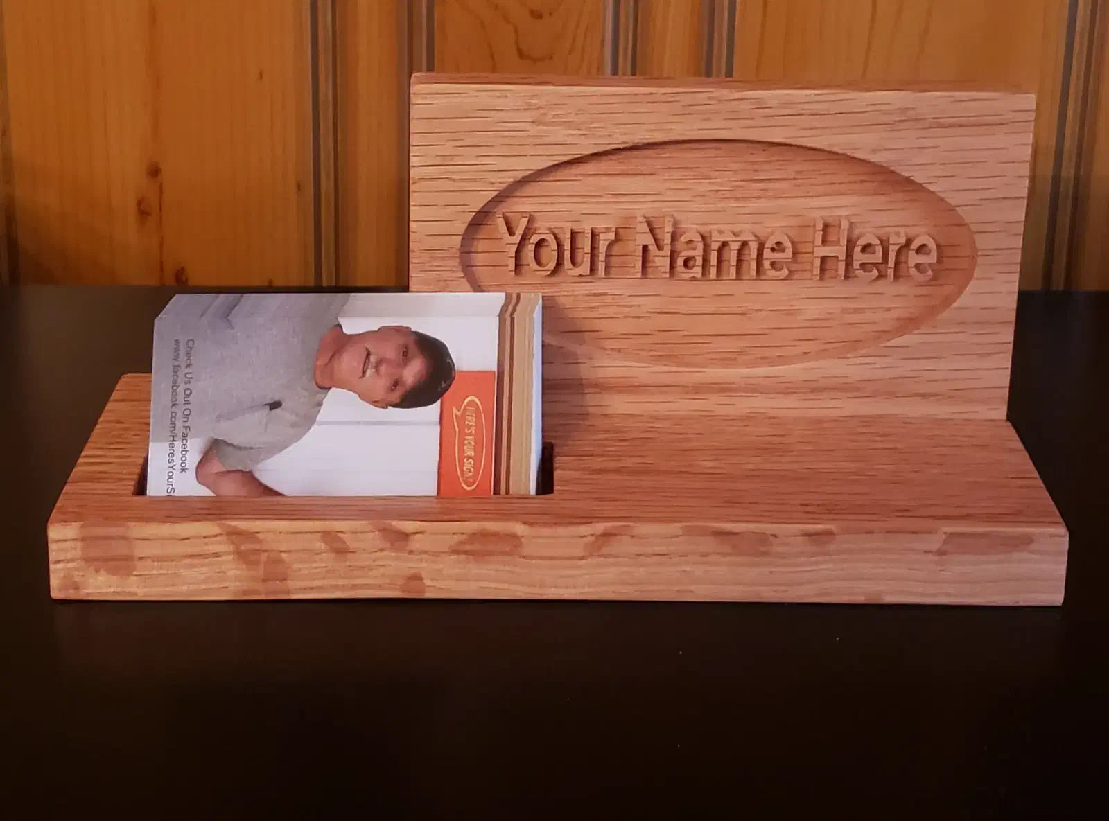 A wooden desktop nameplate with carved placeholder lettering and business cards in a slot on the base