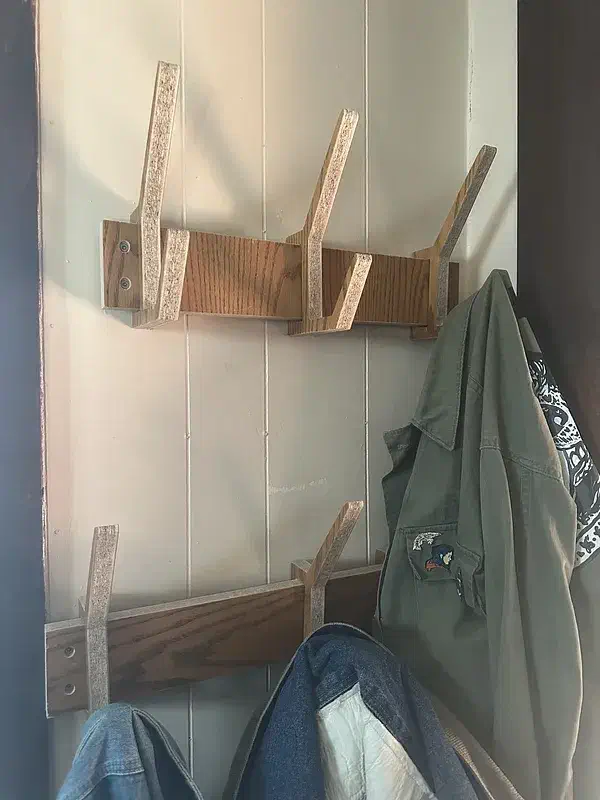 Two wooden wall rails with angled plywood hooks holding a green jacket and a bag