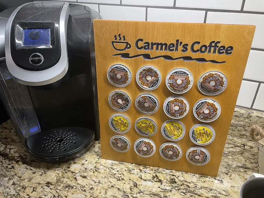 A wooden board holding sixteen coffee pods beside a Keurig machine
