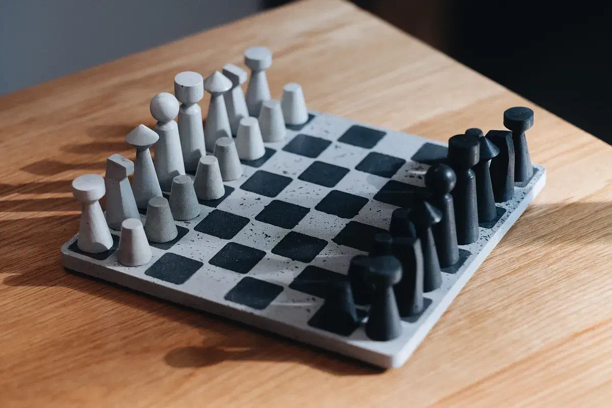 Finished chess set with pale and dark concrete pieces on a matching square board, resting on a wooden tabletop