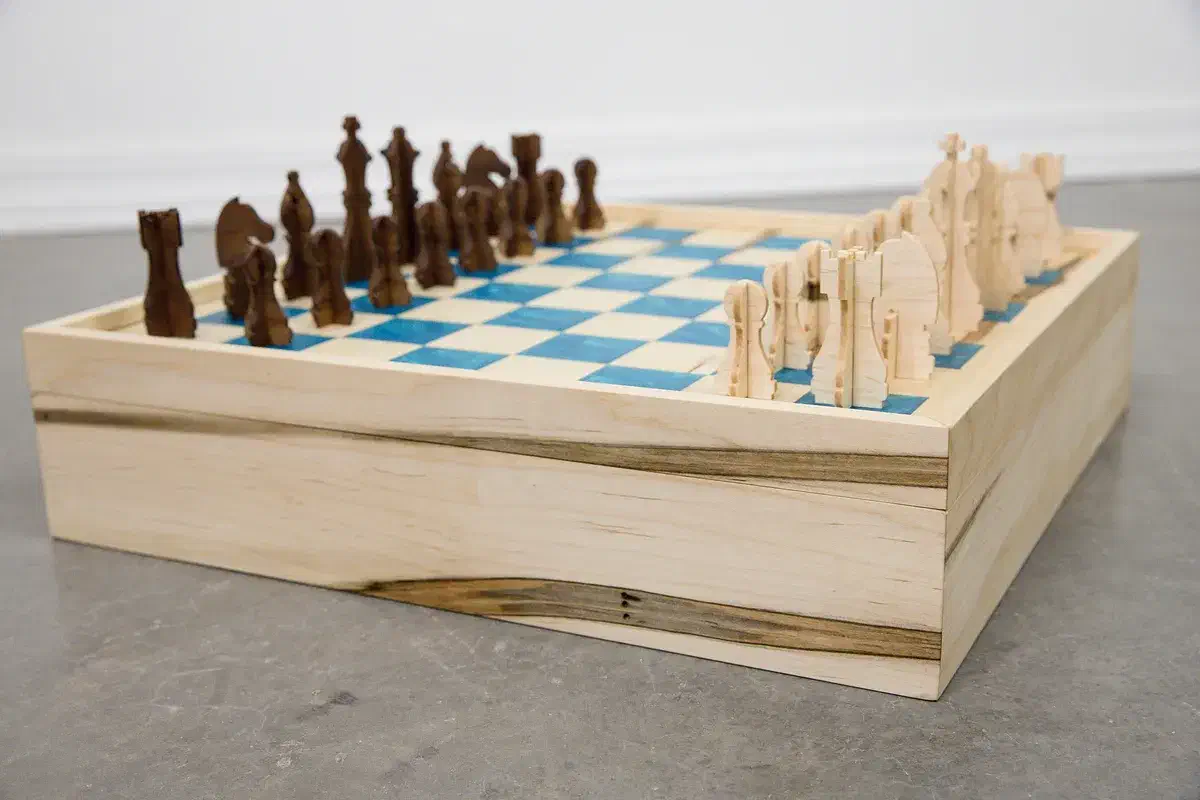 Finished chess and checkers game box with natural and dark wooden pieces arranged on a blue-inlay board