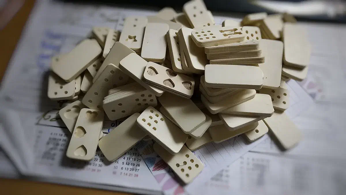 A pile of pale wooden dominoes with carved dots and heart symbols on a printed sheet