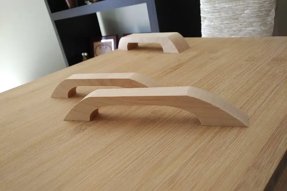 Three finished pale maple drawer pulls arranged on a wooden table