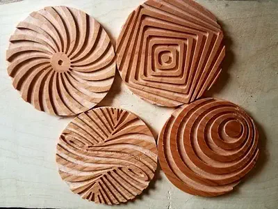Four finished wooden coasters with carved spiral and stepped geometric grooves