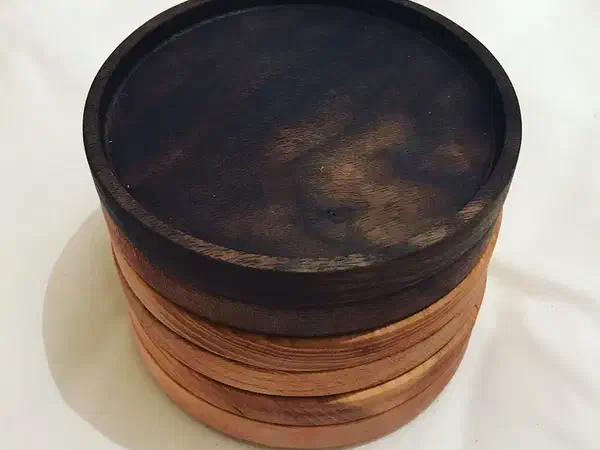 Stack of round hardwood coasters with shallow rims and a dark top coaster