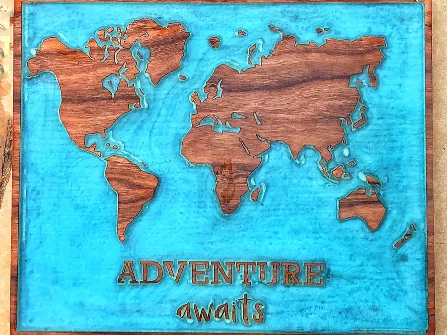 Finished wooden world map with blue epoxy oceans and Adventure awaits lettering