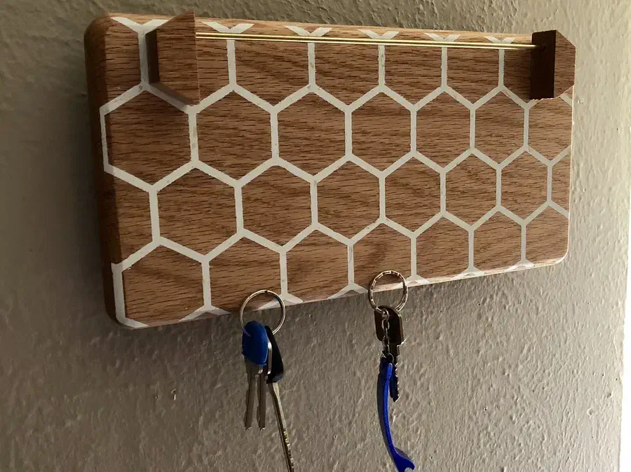 A honeycomb-pattern wooden wall organizer with projecting sunglasses supports, two hanging key rings and a narrow mail slot