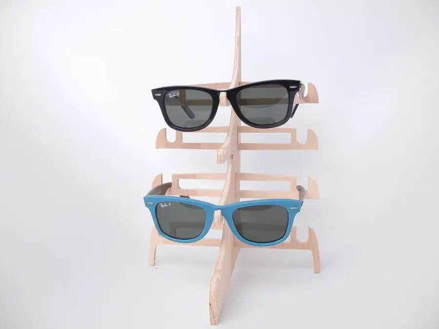 A pale wooden freestanding rack holding black and turquoise sunglasses
