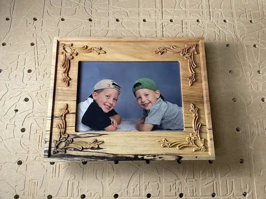 A carved wooden picture frame with floral corners holding a photograph of two children
