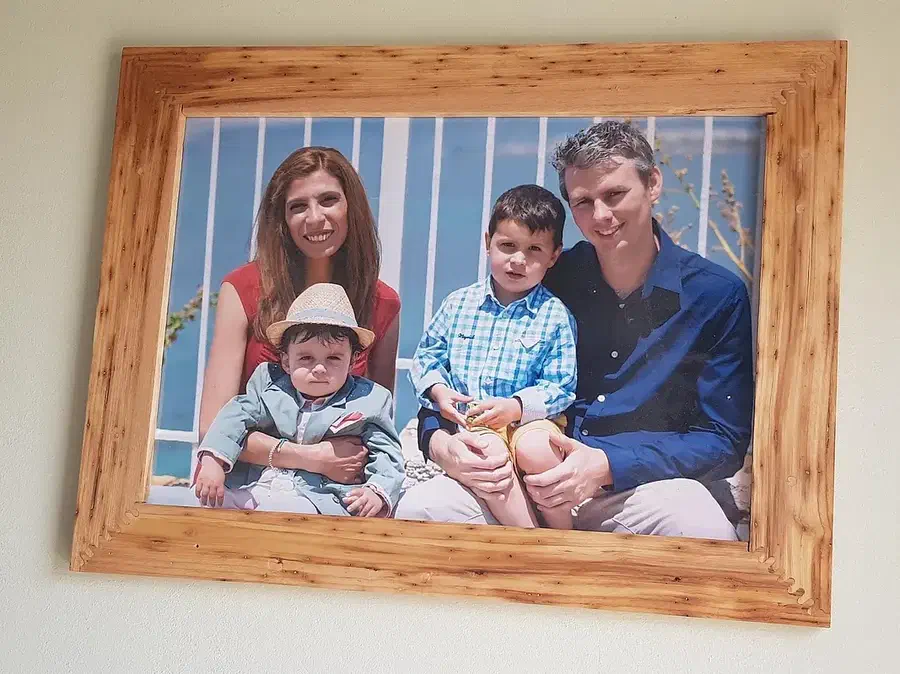A wooden family-photo frame with finger joints at the corners hanging on a wall