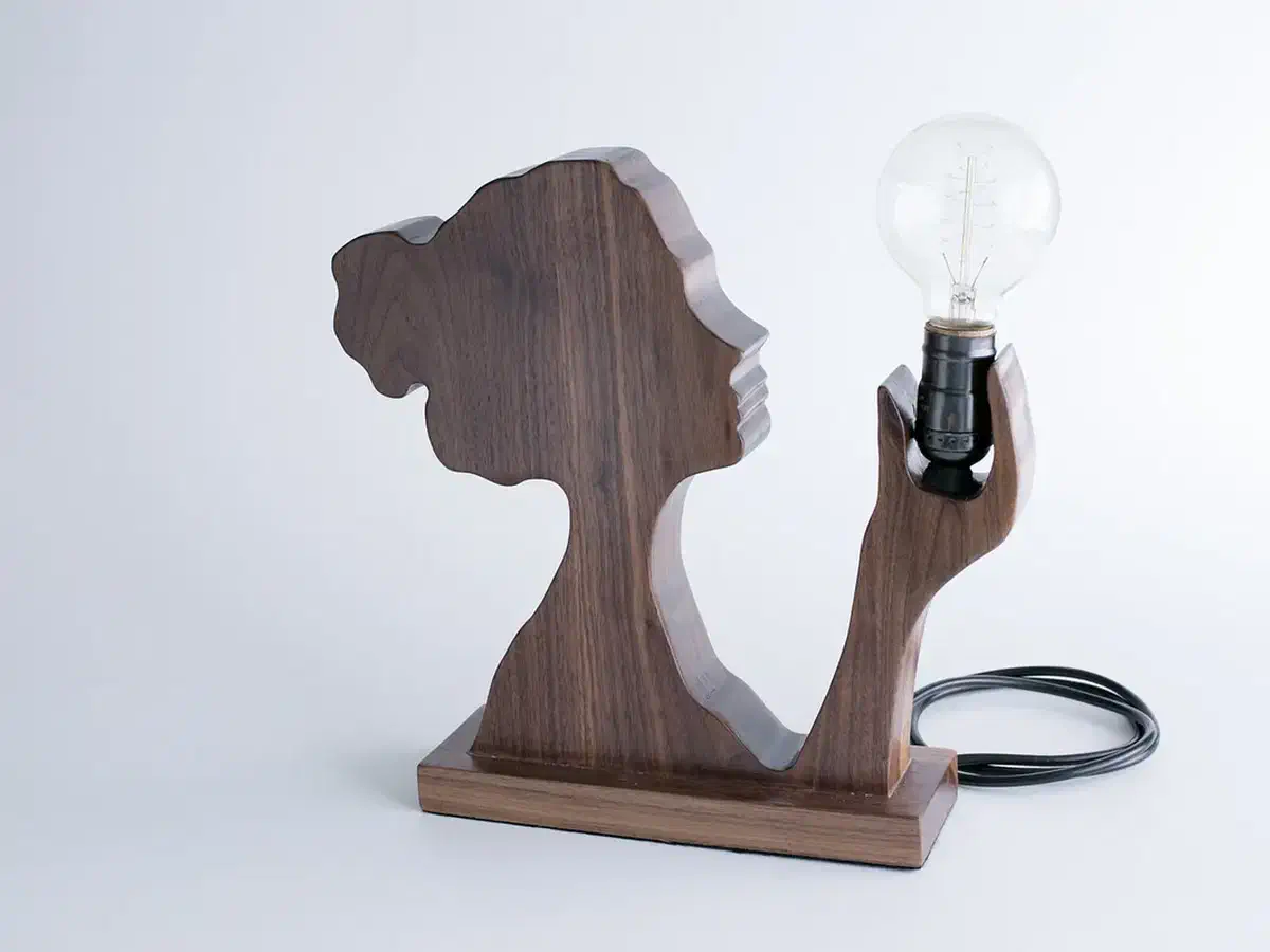 A finished walnut silhouette lamp with a clear bulb and coiled cord against a plain pale background