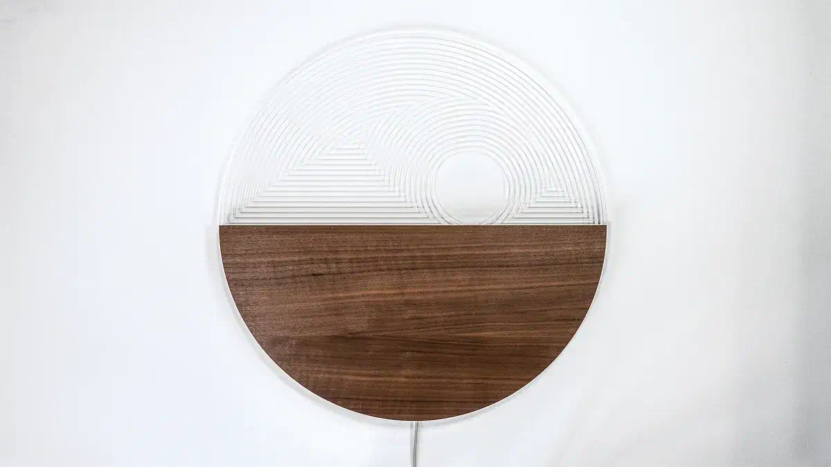 A circular wall lamp with a walnut lower half and an engraved clear acrylic upper half