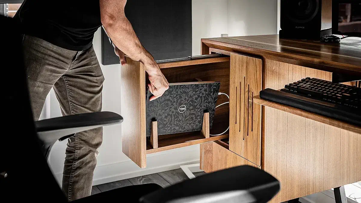 A laptop held vertically inside a wooden desk drawer with cables beside it