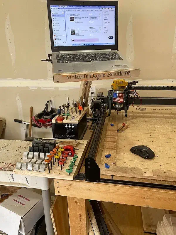 A laptop on a plywood arm above a CNC controller with separate clamp and router-bit storage boards