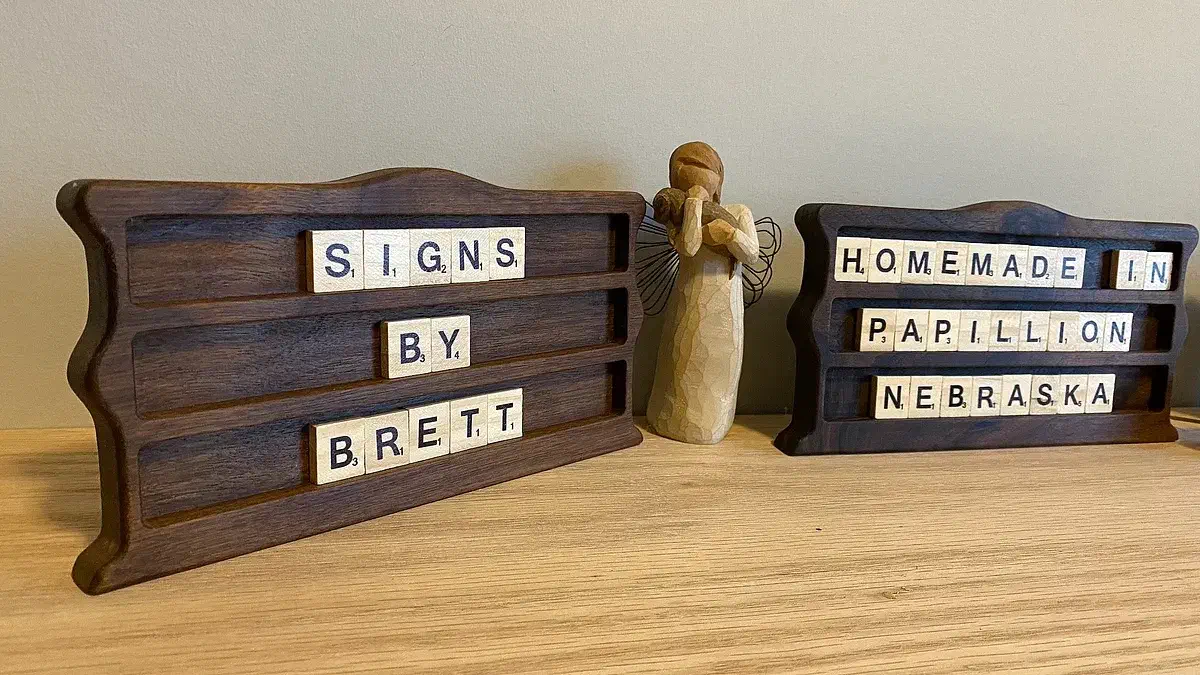 Two walnut tabletop displays holding letter tiles that spell Signs By Brett and Homemade In Papillion Nebraska