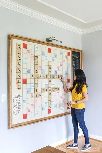A woman placing a letter tile on a large framed wooden wall game in a room