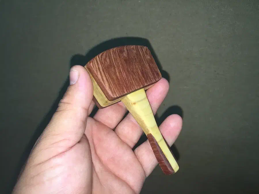 A hand holding a miniature laminated wooden mallet with a dark curved head and pale handle
