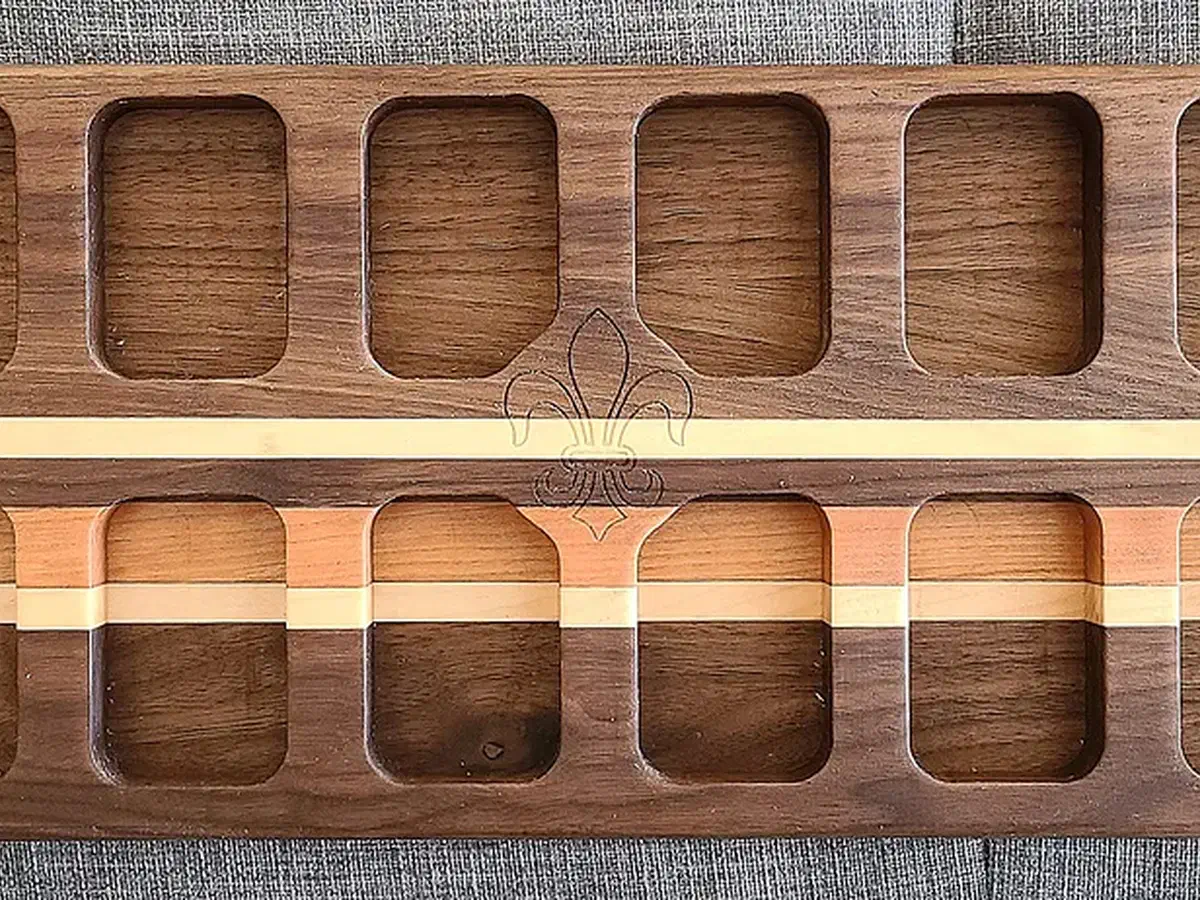 Walnut Mancala board with rows of rectangular pockets, light wood inlay strips, and a bag of game stones resting over one end