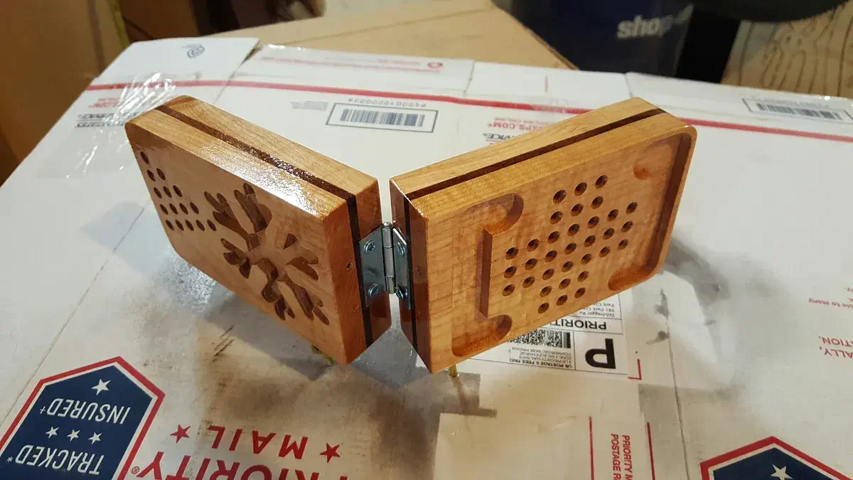 Hinged maple game case with drilled game holes and a carved starburst, photographed on shipping packaging