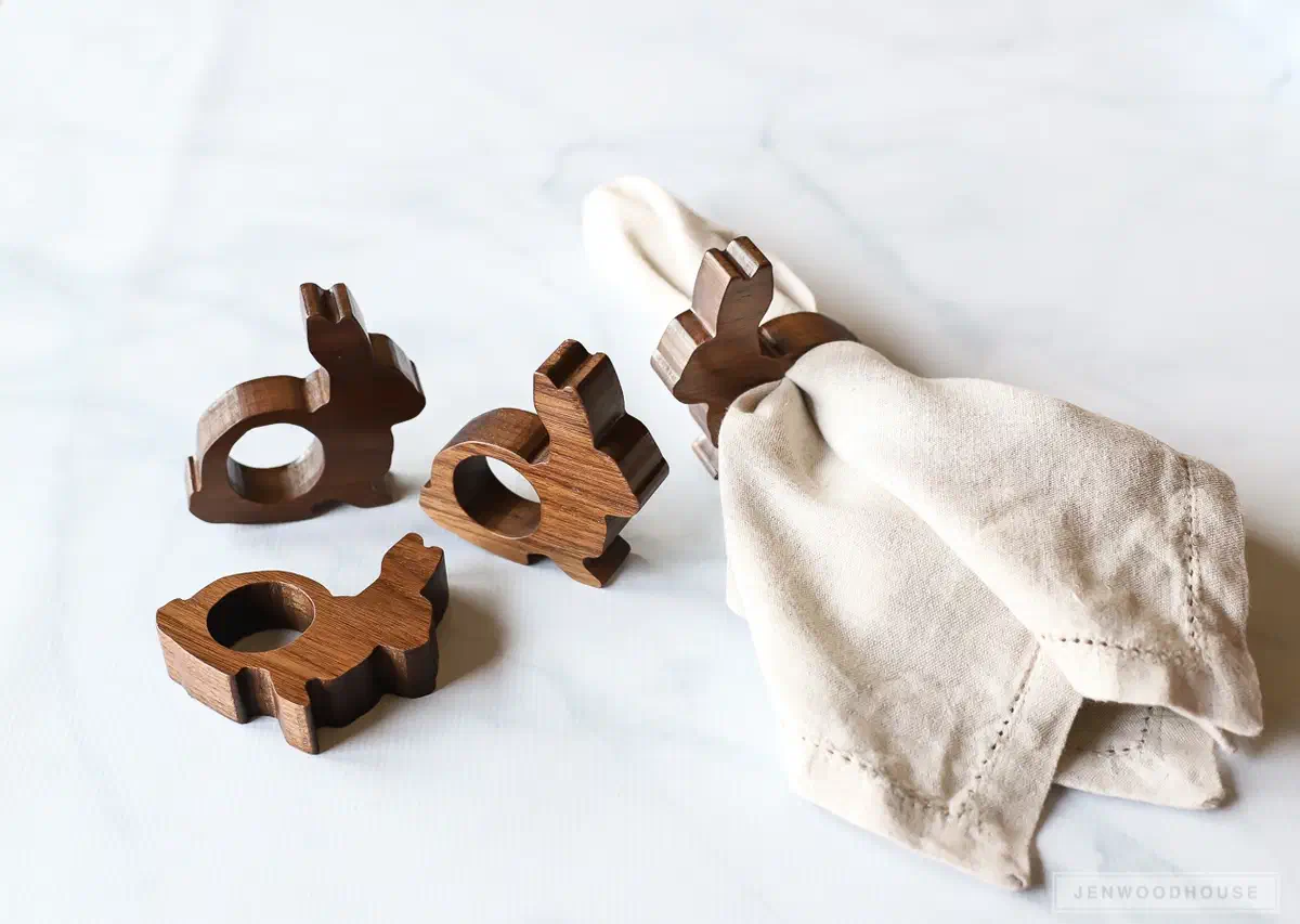 Walnut bunny-shaped napkin rings beside a gathered cream napkin on a pale tabletop