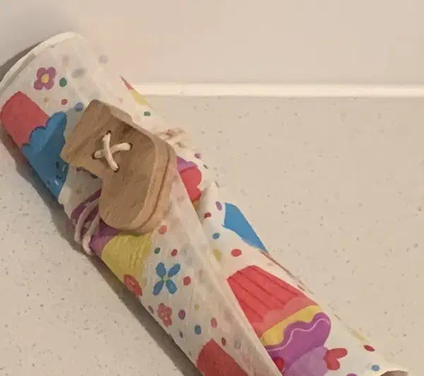 A wooden Christmas stocking button tied around a rolled patterned napkin with white cord