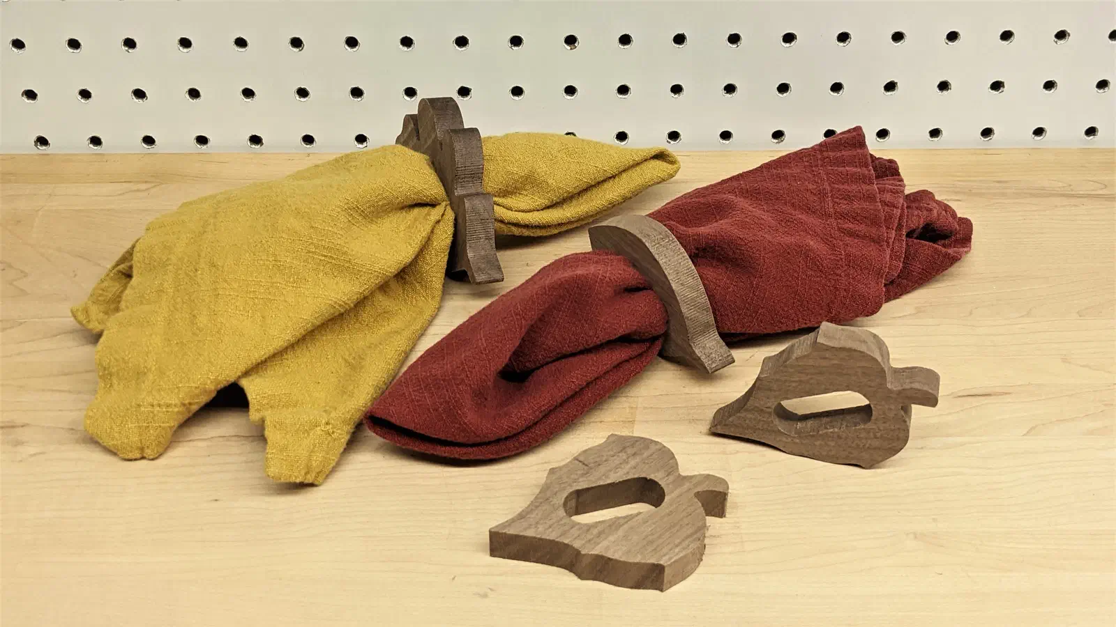 Leaf-shaped wooden napkin rings holding yellow and burgundy napkins, with two loose rings on a workbench