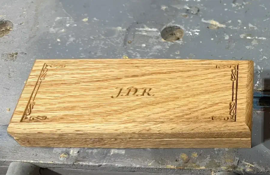 A closed oak pencil case with carved J.D.R. initials and a decorative border on its lid