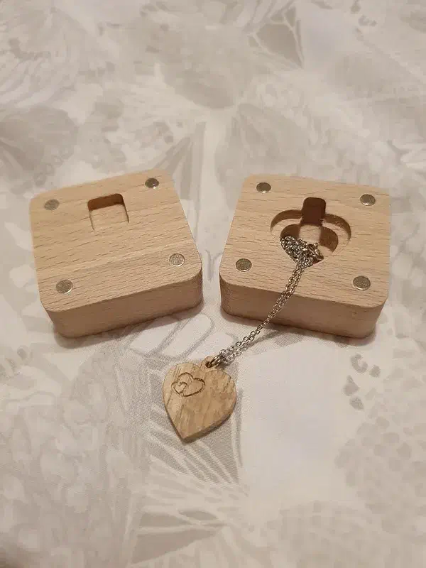 An oak heart pendant and chain beside two wooden gift-box halves with round magnets