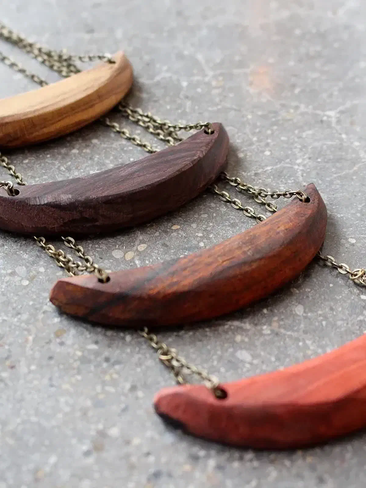 Four curved wooden necklace pendants in pale, dark and reddish wood with metal chains