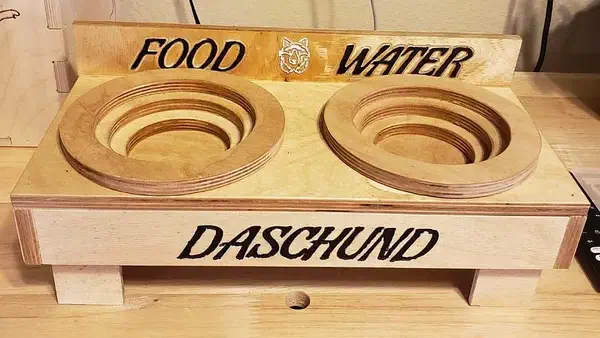 A complete birch-plywood dog feeder with two stacked wooden bowls, FOOD and WATER lettering on the back and DASCHUND lettering across the front.