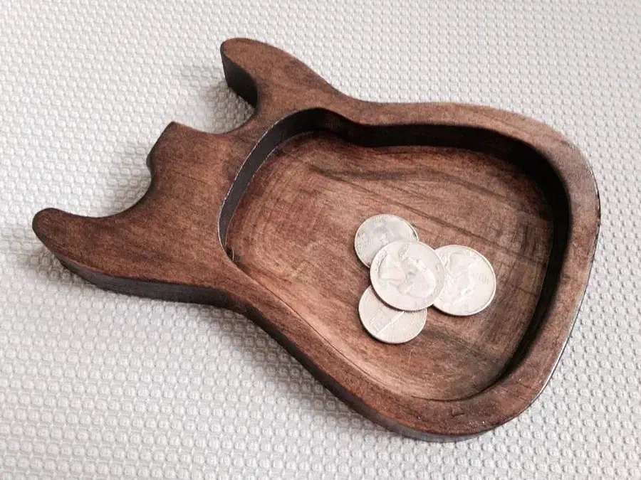 A dark wooden guitar-body tray with a recessed center holding several coins