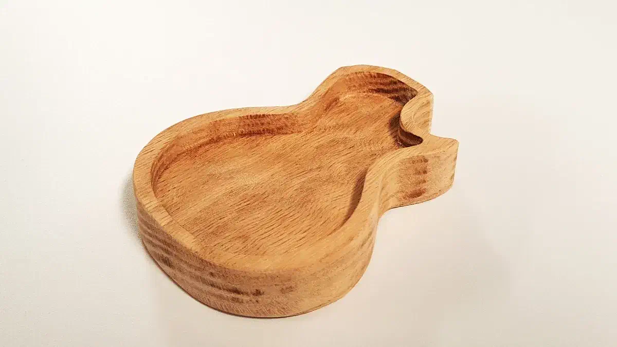 A finished wooden pick tray with a single-cutaway guitar outline and a recessed center