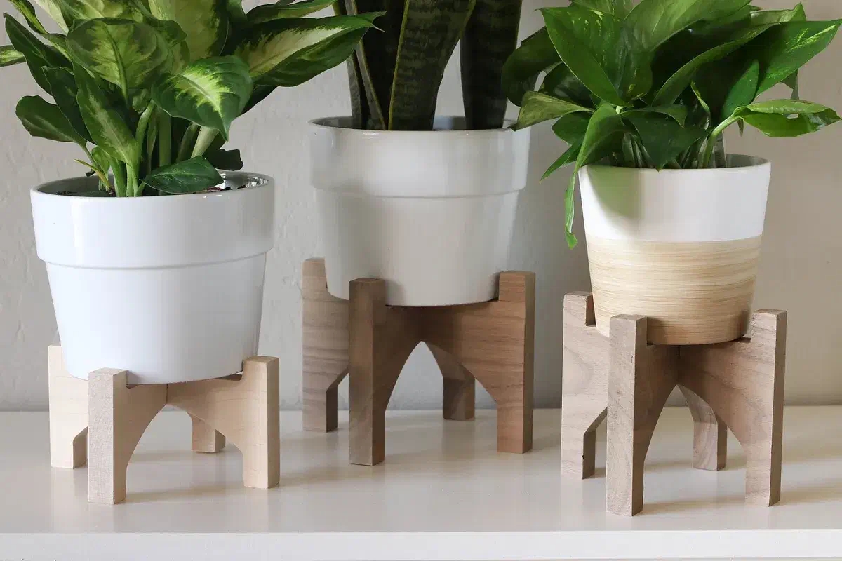 Three small wooden stands supporting white plant pots, with arched openings beneath the pots
