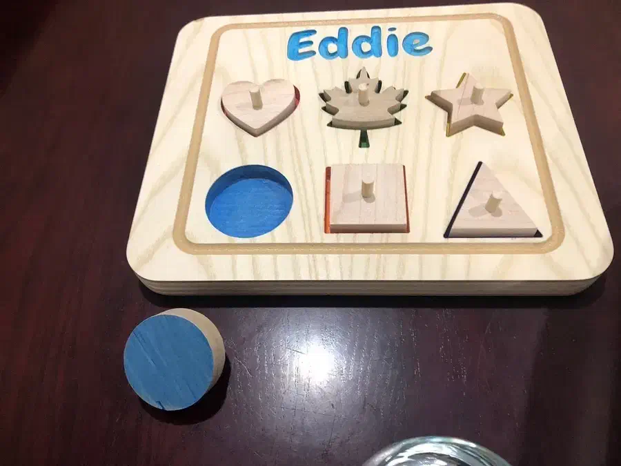 Wooden shape puzzle with fitted heart, maple leaf, star, square and triangle pieces and a blue circular piece beside the board