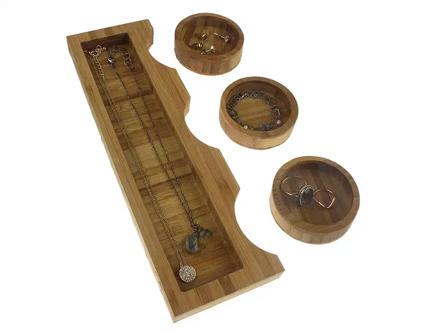 A bamboo tray beside three removable round bowls holding rings, earrings and a bracelet