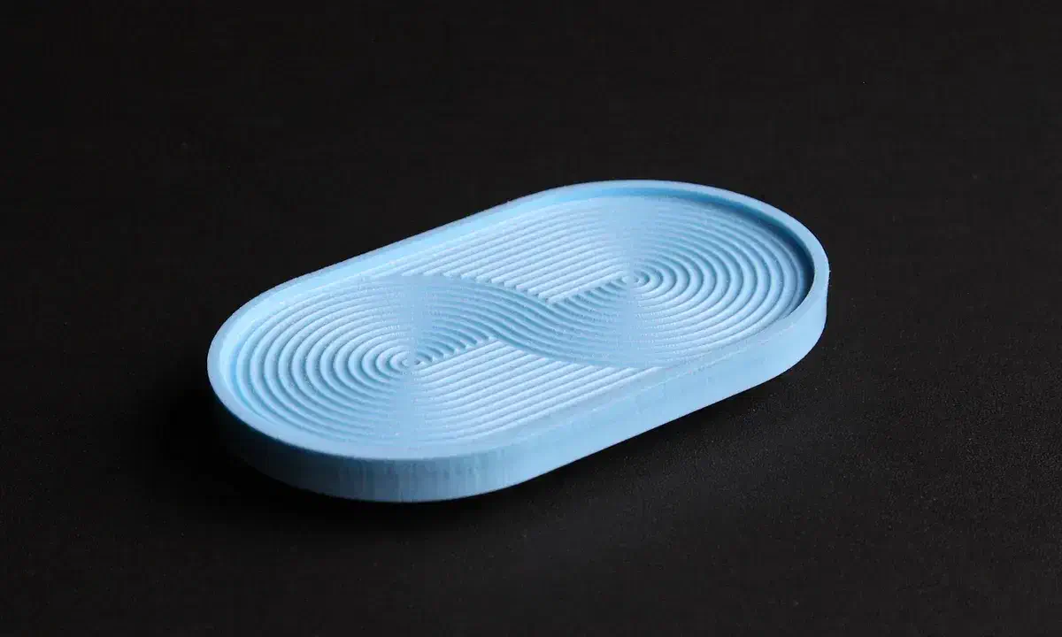 A finished blue oval HDPE soap dish with curved concentric channels on a dark surface