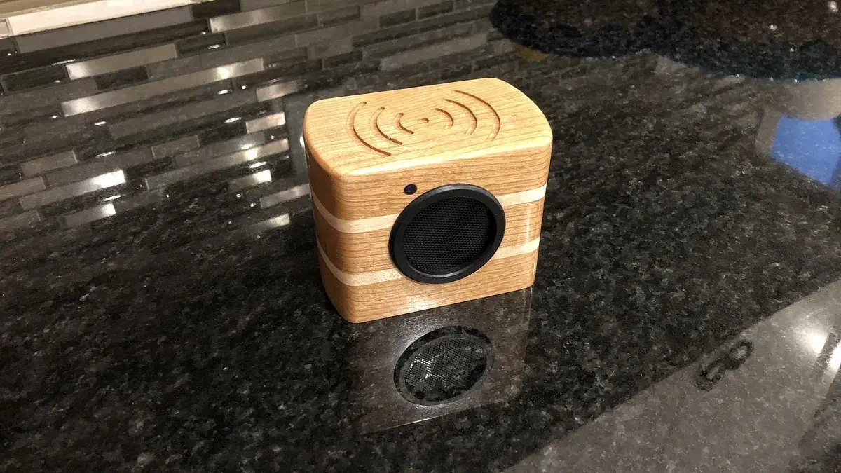 A small wooden speaker with a dark round grille and a pale stripe standing on a dark countertop