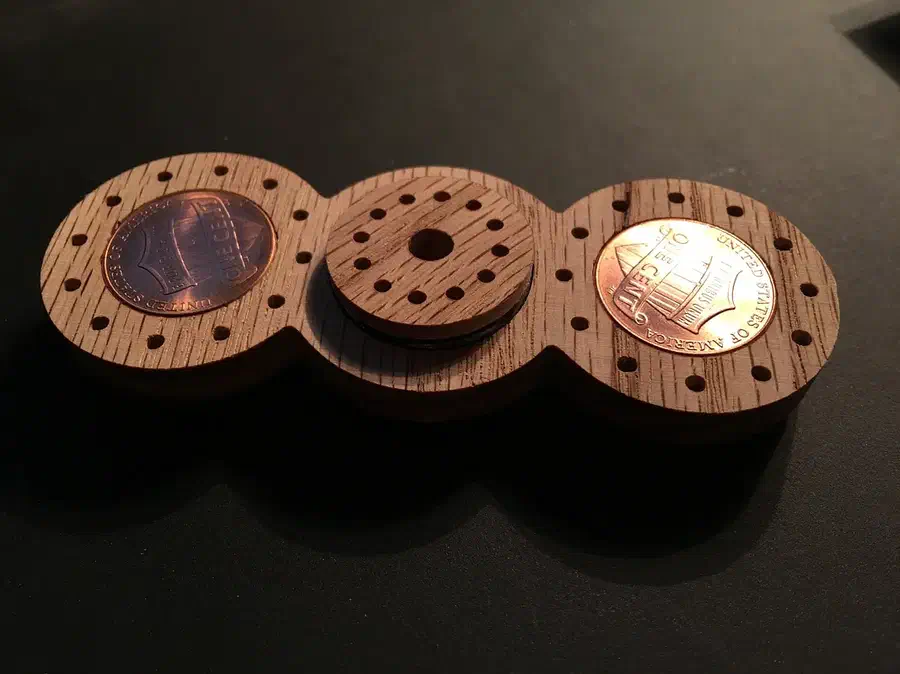 An oak bar-shaped spinner with pennies at both ends, drilled decoration and a wooden center cap
